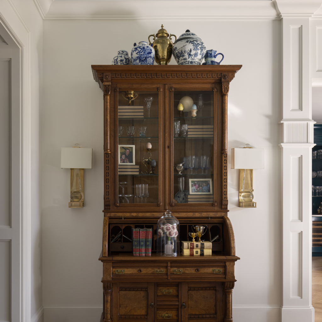 Wooden china cabinet with glass doors displaying various items in a room with white walls and a door.