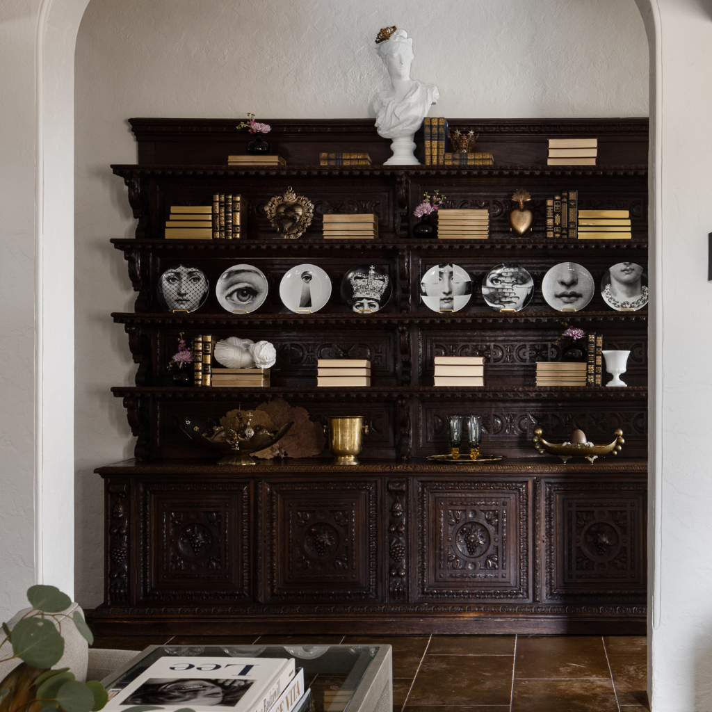 Decorative shelf with various items including books, plates, and sculptures in a room.