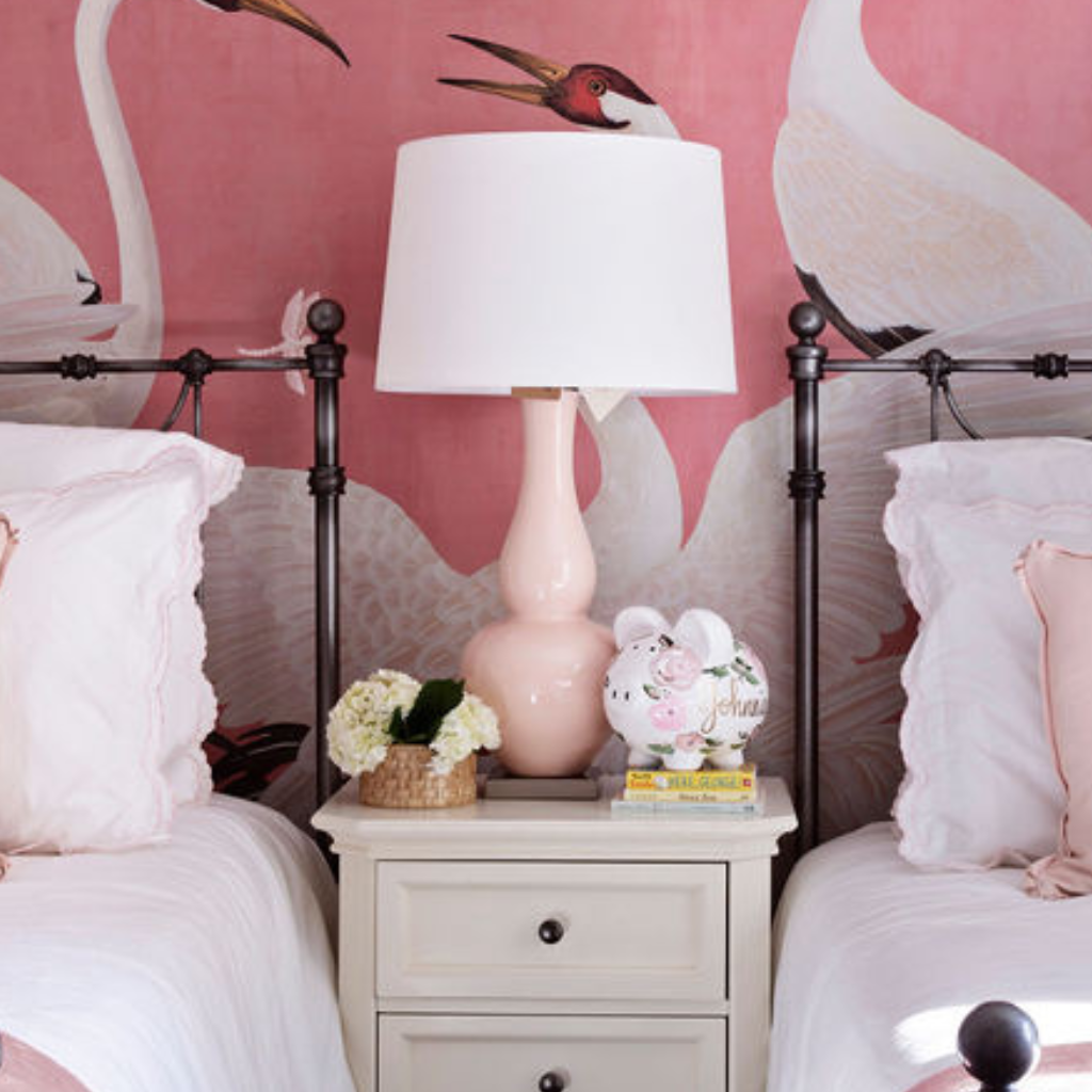 Two beds with pink lamps and decorative items against a pink wall with bird illustrations.